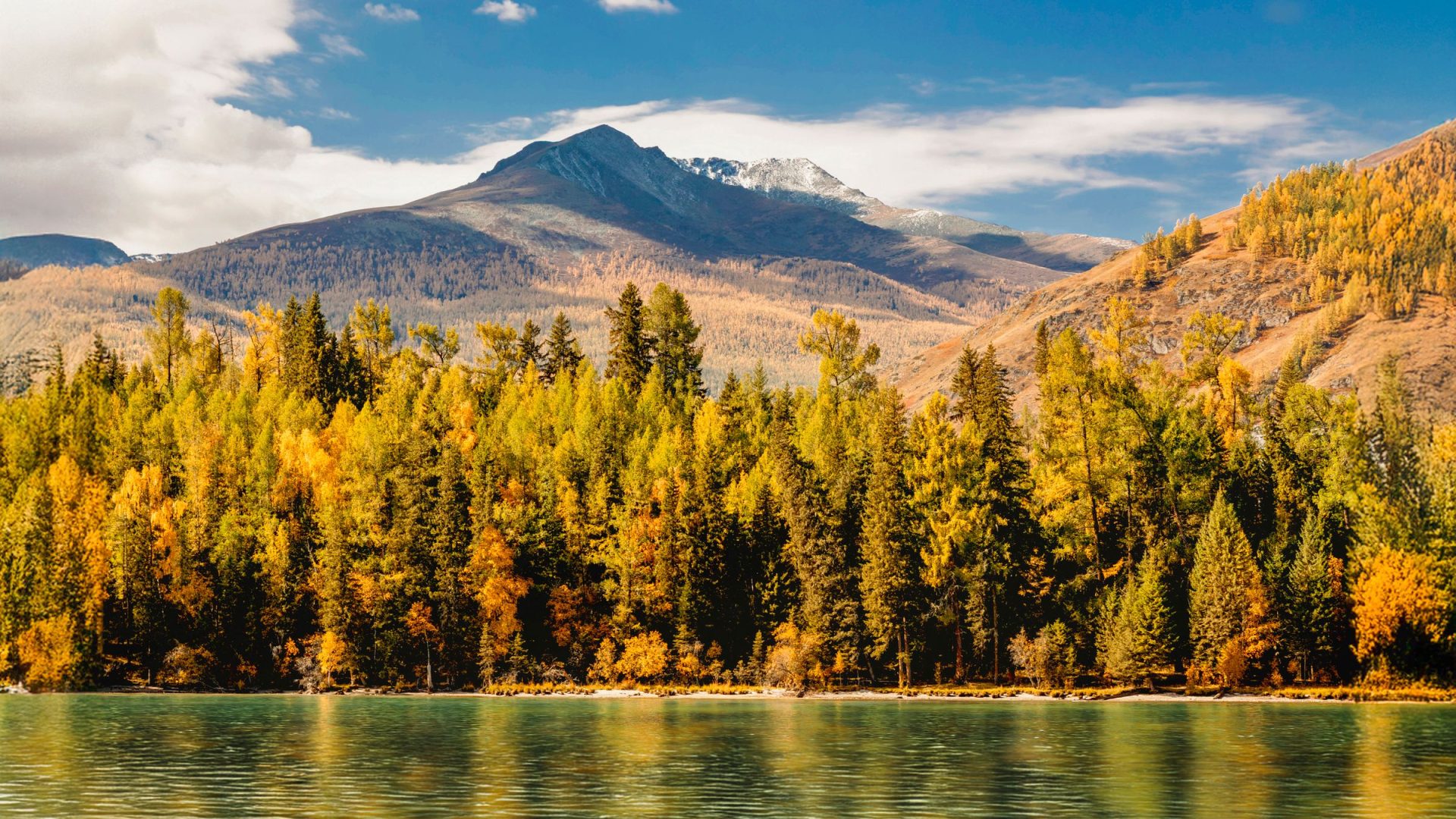 Golden autumn trees along a lake beneath a mountain range