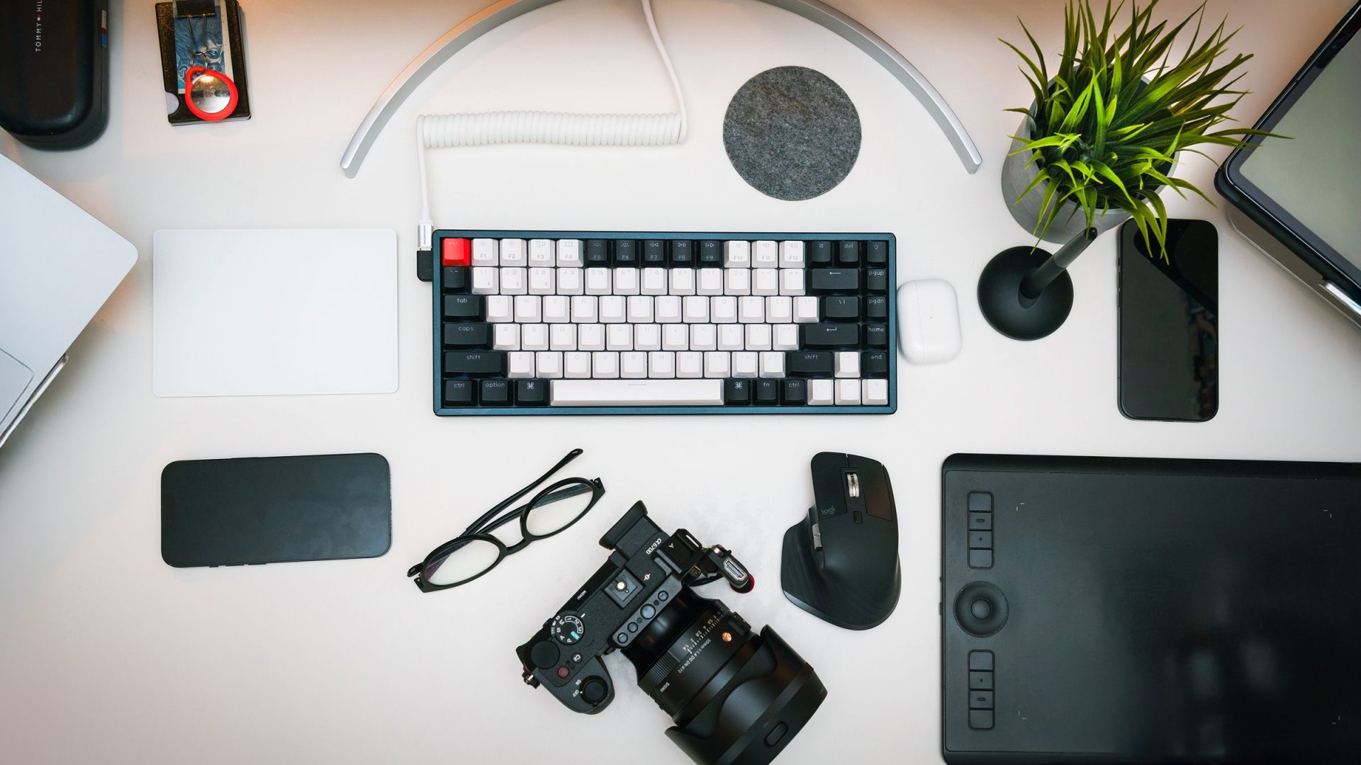 Camera and pen tablet on a clean white photo-editing desk with a keyboard and plant