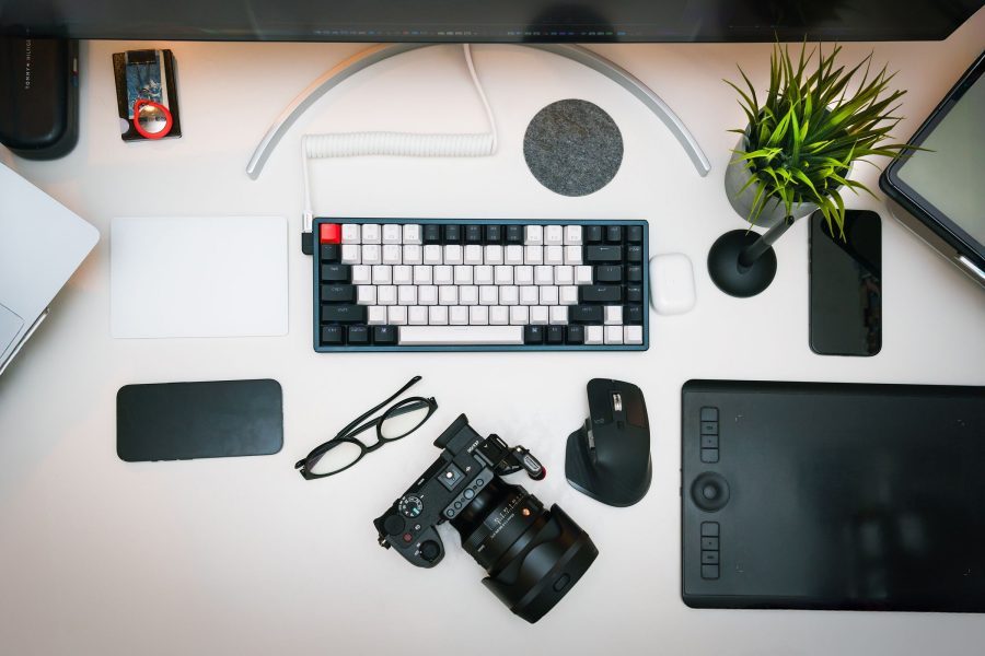 Camera and pen tablet on a clean white photo-editing desk with a keyboard and plant