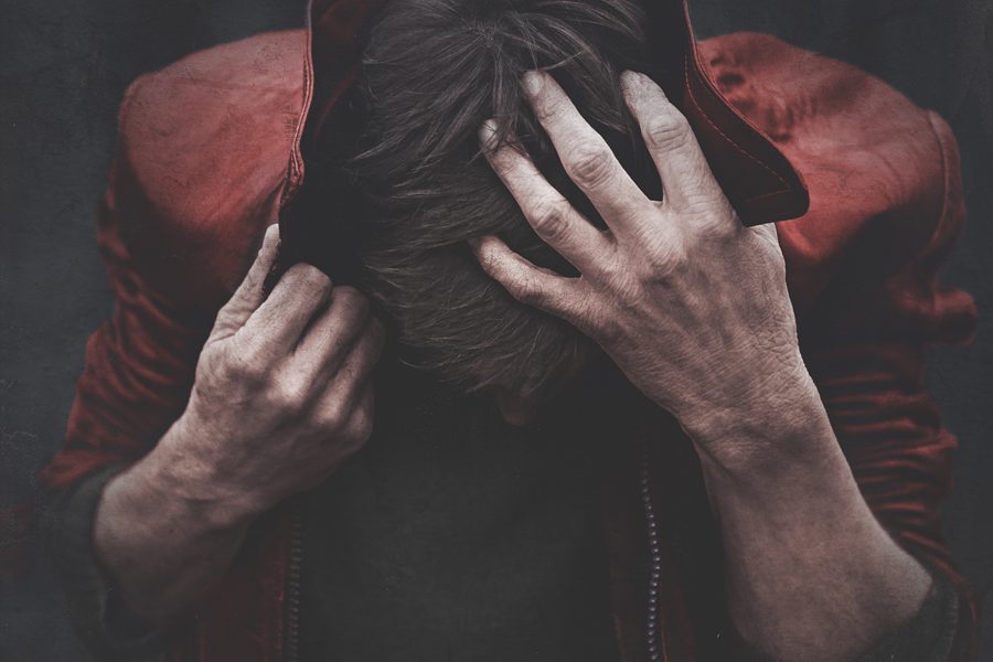 Person in a red jacket bends forward with hands covering their head.