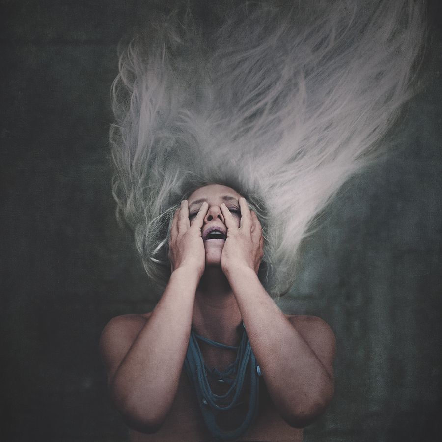 Portrait of a person holding their face as pale hair rises above them.