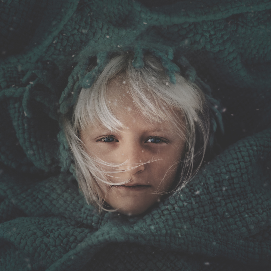 Child’s face surrounded by dark green textured fabric.