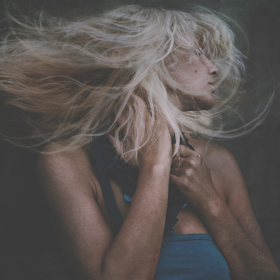 Portrait of a person with long pale hair blowing across their face.