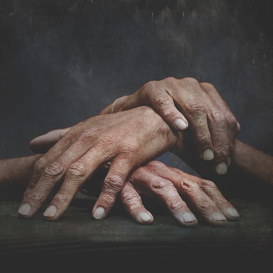 Close-up of three hands overlapping against a dark background.