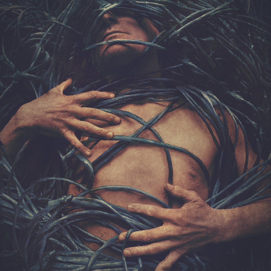 Person lying among leaves and grass, with hands resting across a bare torso.