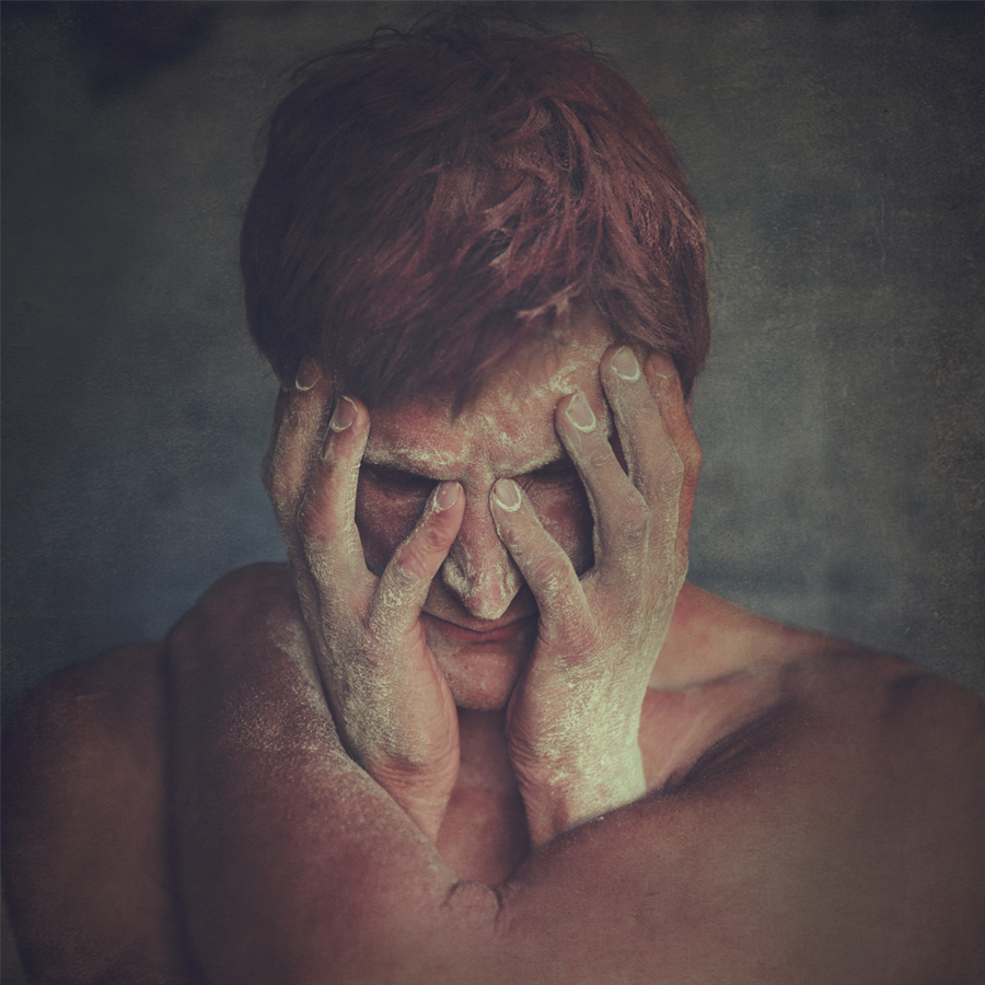 Person with short red hair covers their face with both hands.
