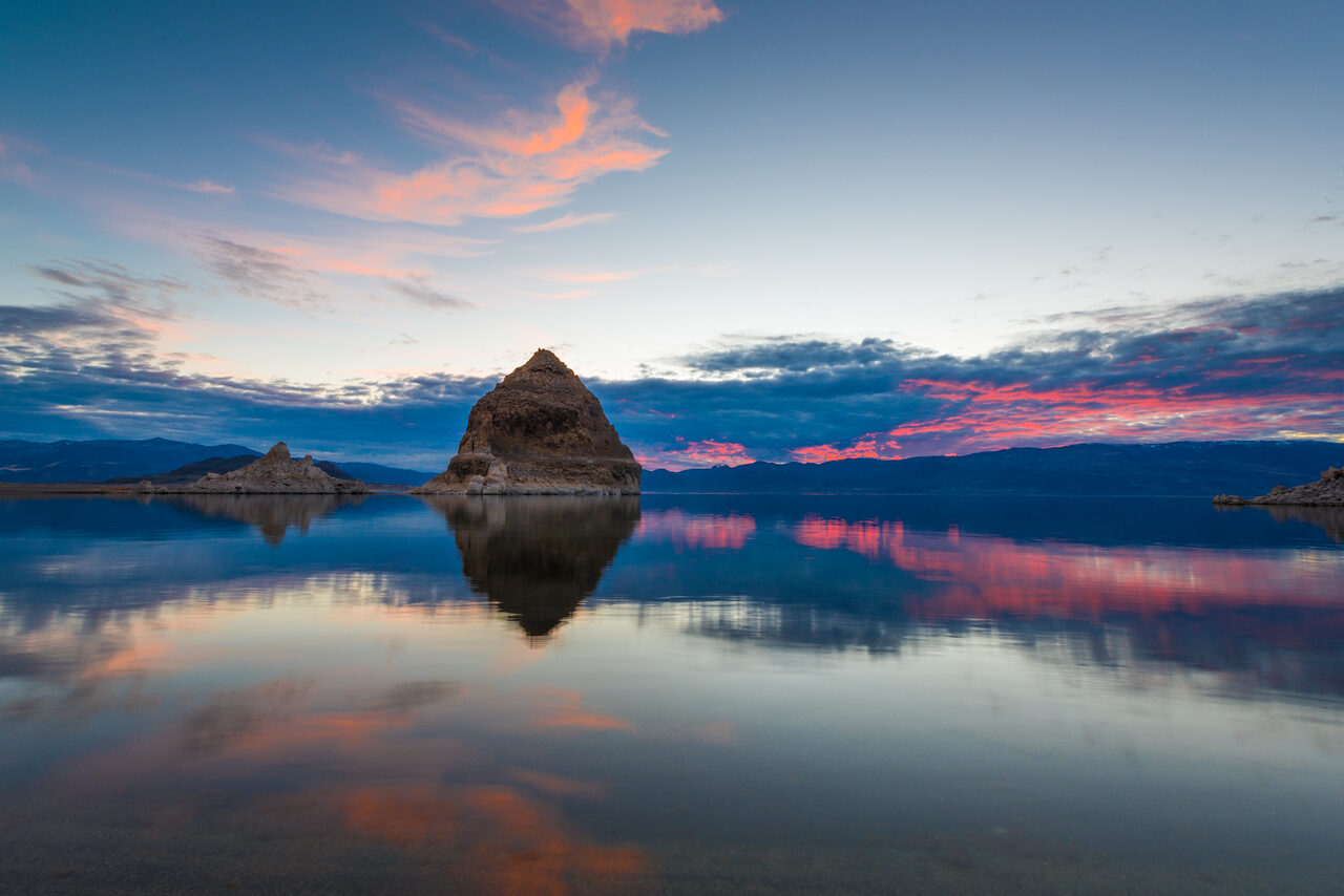 Pyramid-shaped rock reflected in Pyramid Lake at blue hour beneath pink clouds, Nevada.