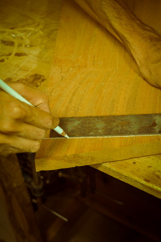 A hand marks a wooden board with a pencil and straightedge.