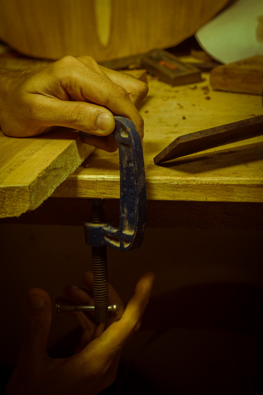 Close-up of a hand tightening a clamp around a wooden piece.