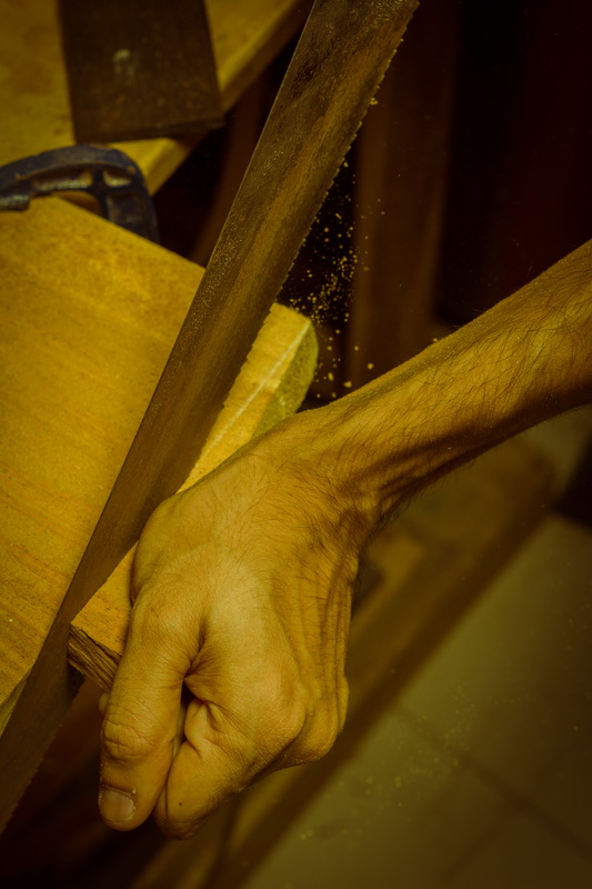 Craftsperson holds a piece of wood beside a woodworking bench.