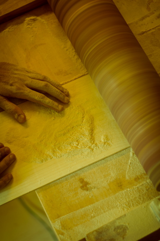 Hands smooth a wooden board beside a sanding drum.