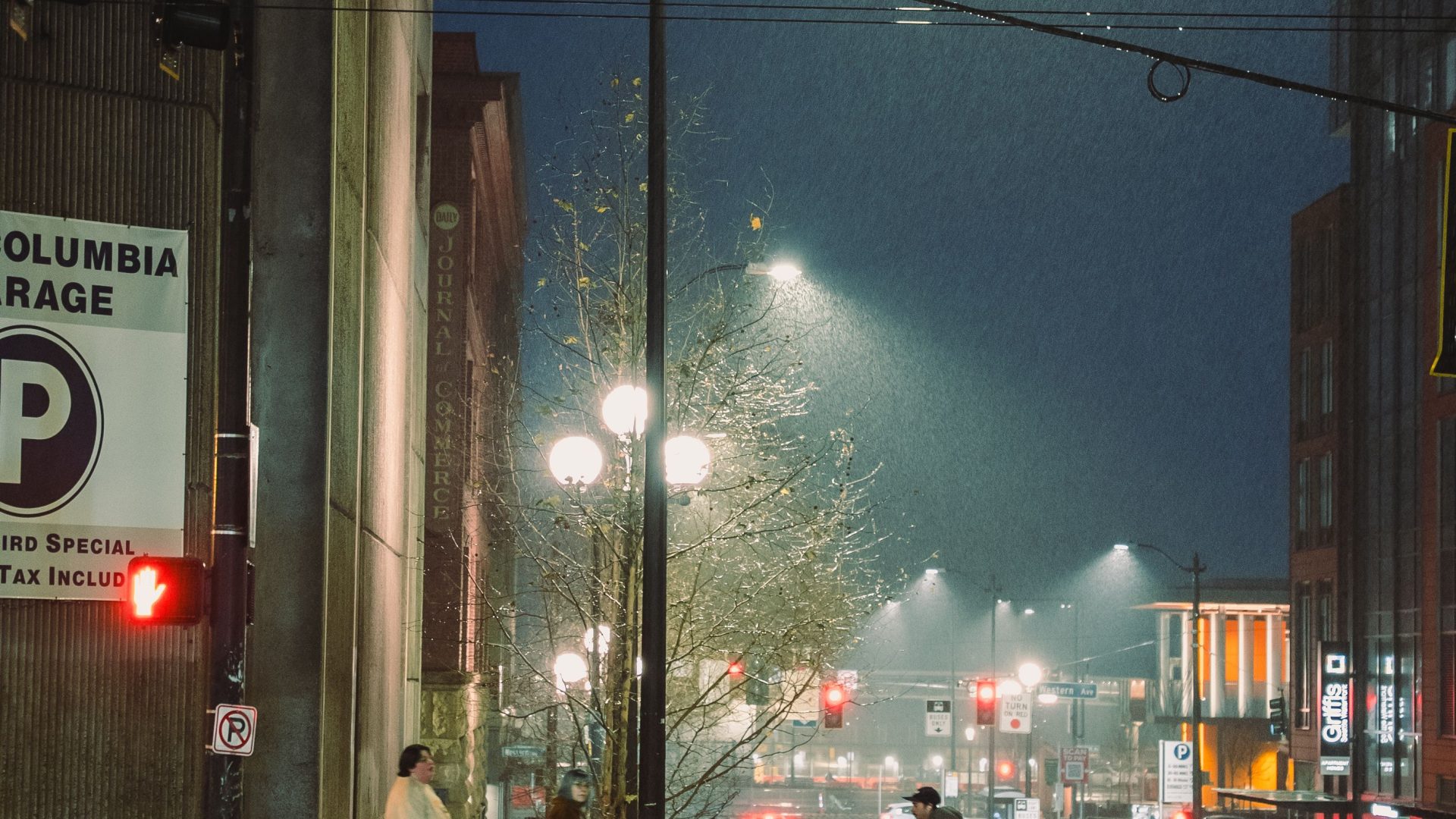 Pedestrians crossing a rain-soaked Seattle street beneath streetlights at night