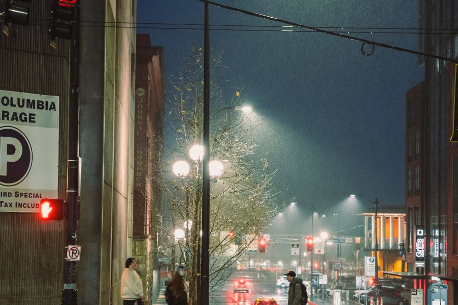 Pedestrians crossing a rain-soaked Seattle street beneath streetlights at night