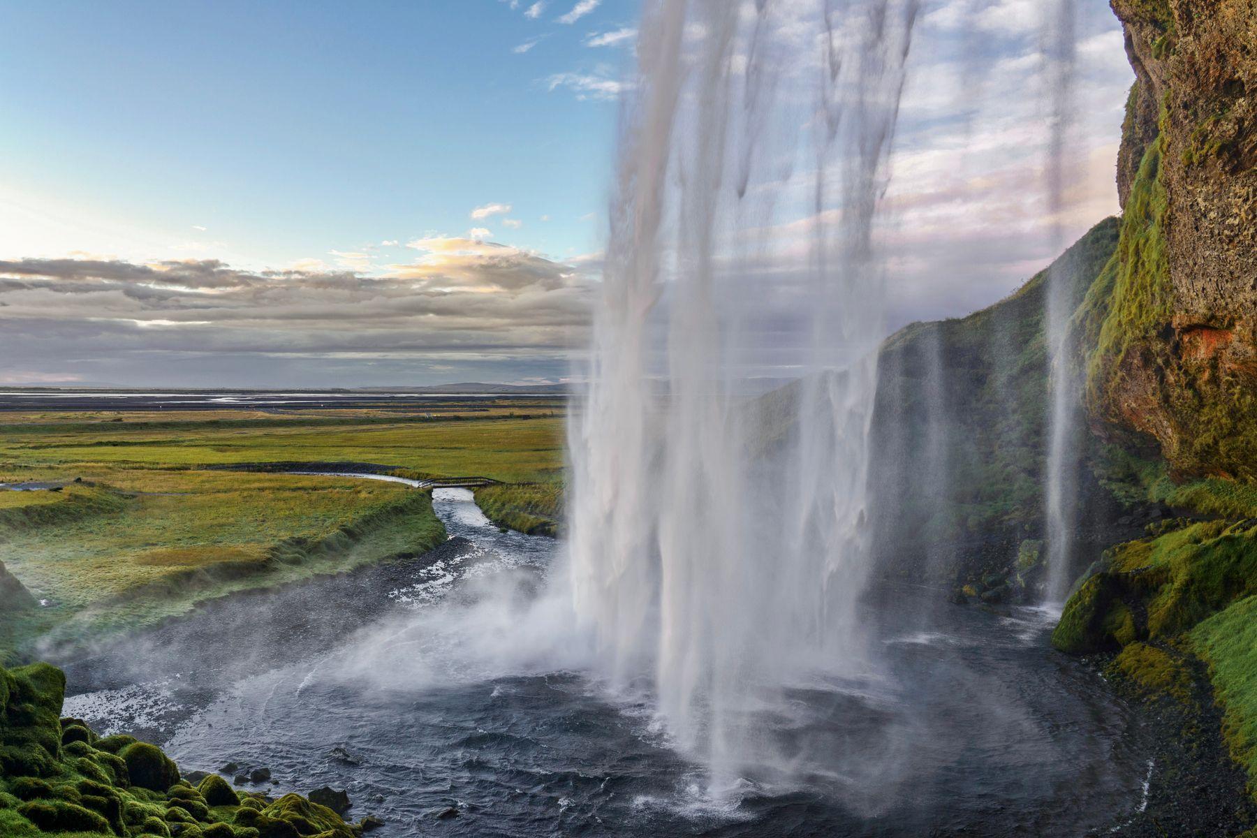 Seljalandsfoss waterfall dropping past a mossy cliff above green Icelandic fields.