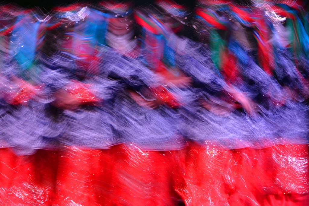 Blurred row of dancers in patterned costumes and red skirts.