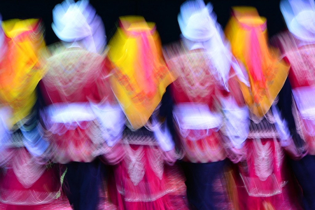 Dancers in red-and-white costumes with yellow scarves blurred in motion.
