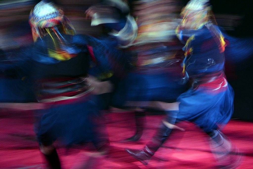 Two performers in blue costumes spin across a red-lit stage.