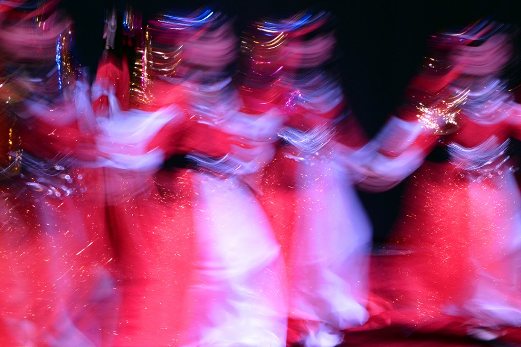 Performers in red and white costumes form a blurred line as they dance.