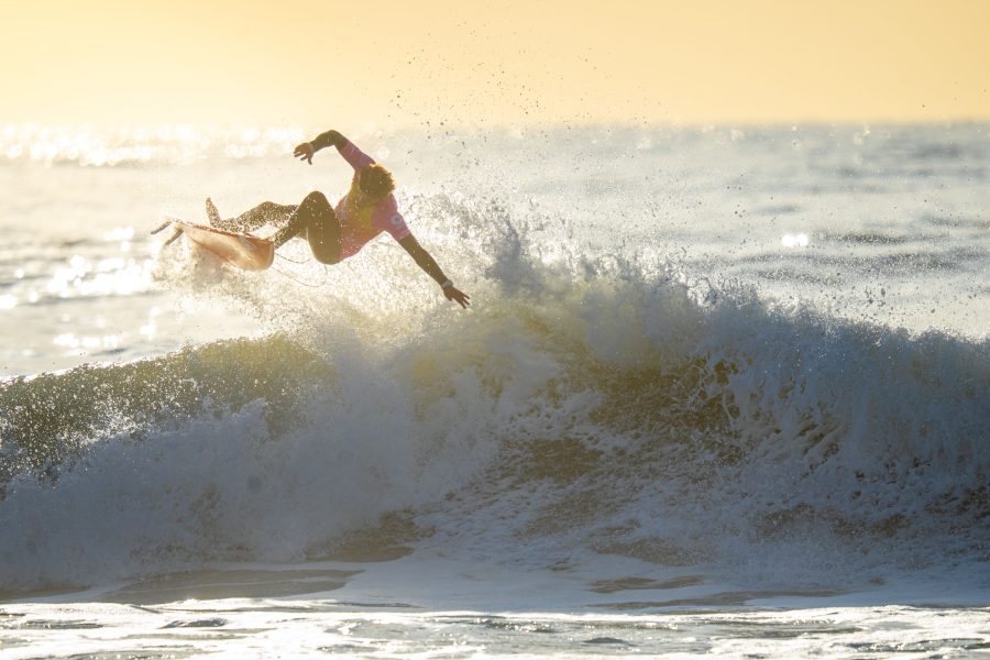 Surfer airborne above a breaking wave in low sunlight