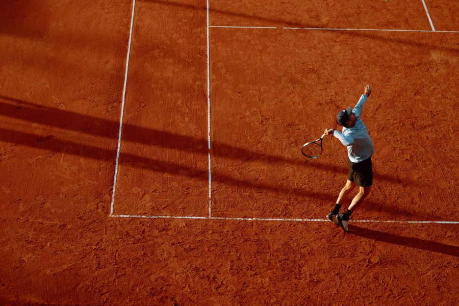 Tennis player serving on a red clay court in low sunlight