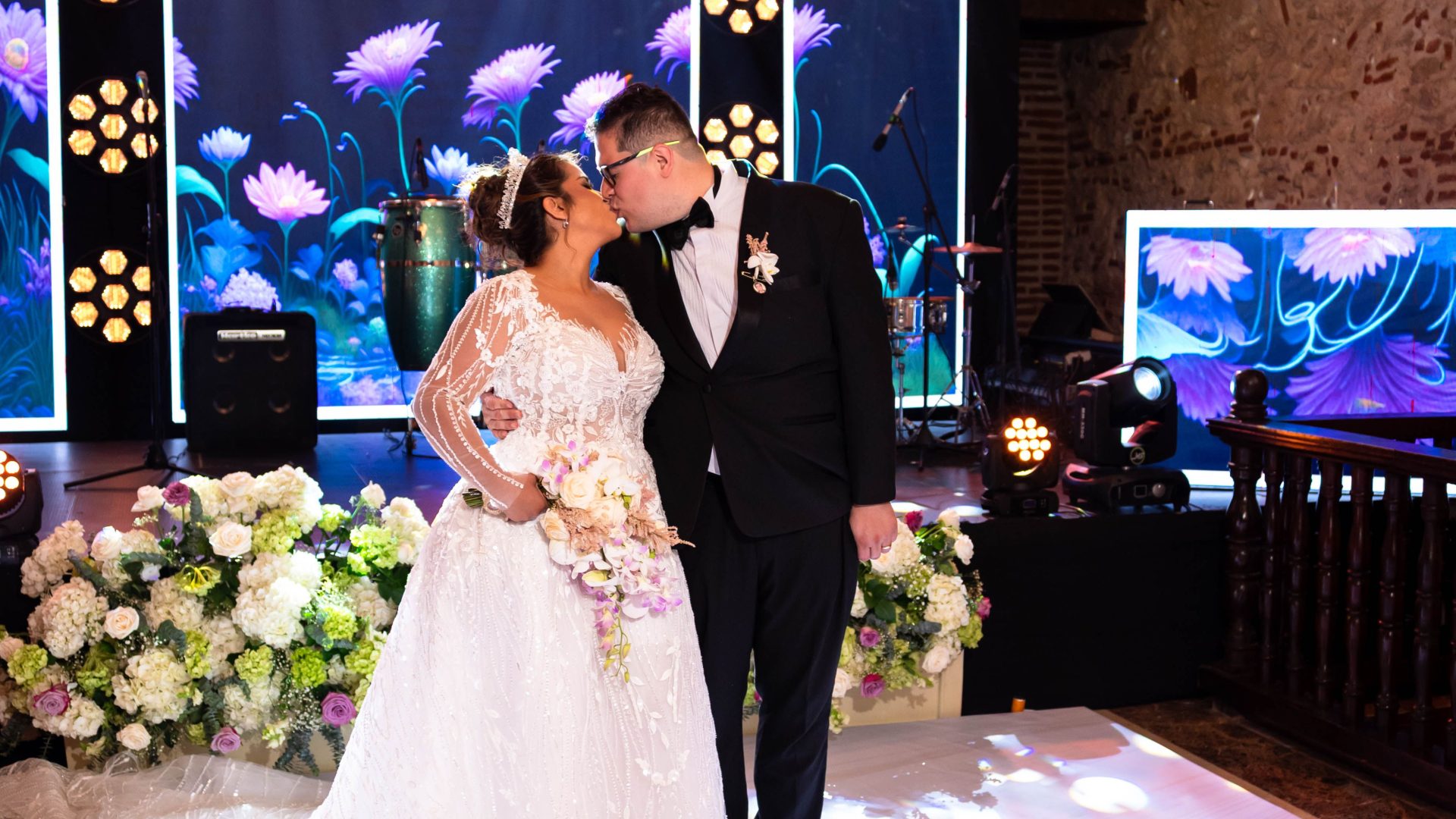 Bride and groom kissing beneath chandeliers and flowers at their reception