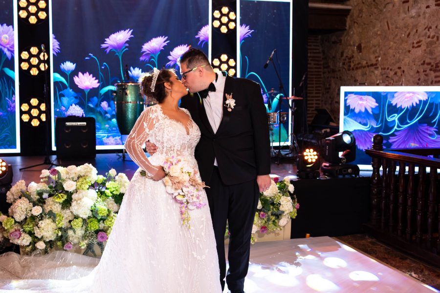 Bride and groom kissing beneath chandeliers and flowers at their reception