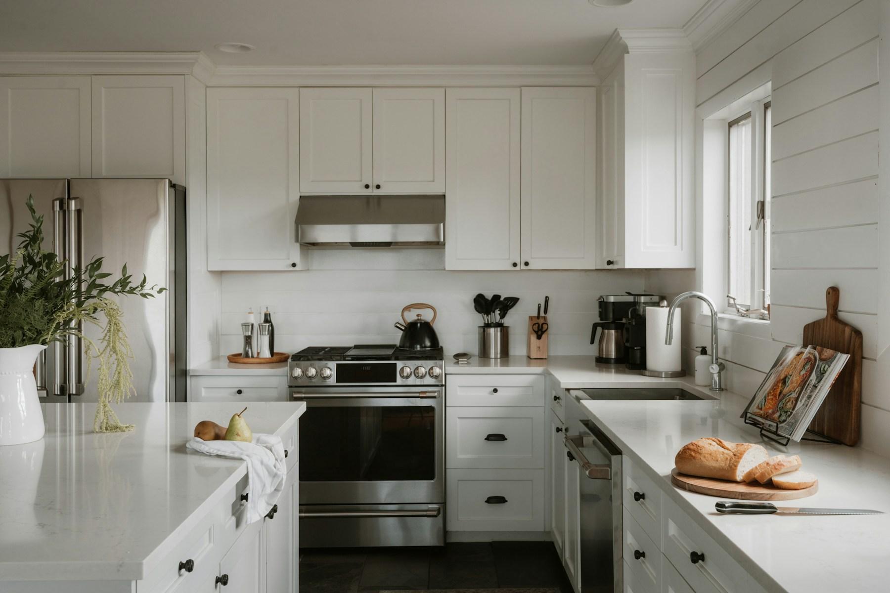 White kitchen with stainless-steel stove, refrigerator, island, and window light.