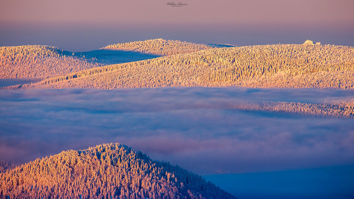 Sunlit snow-covered ridges above a valley filled with clouds.