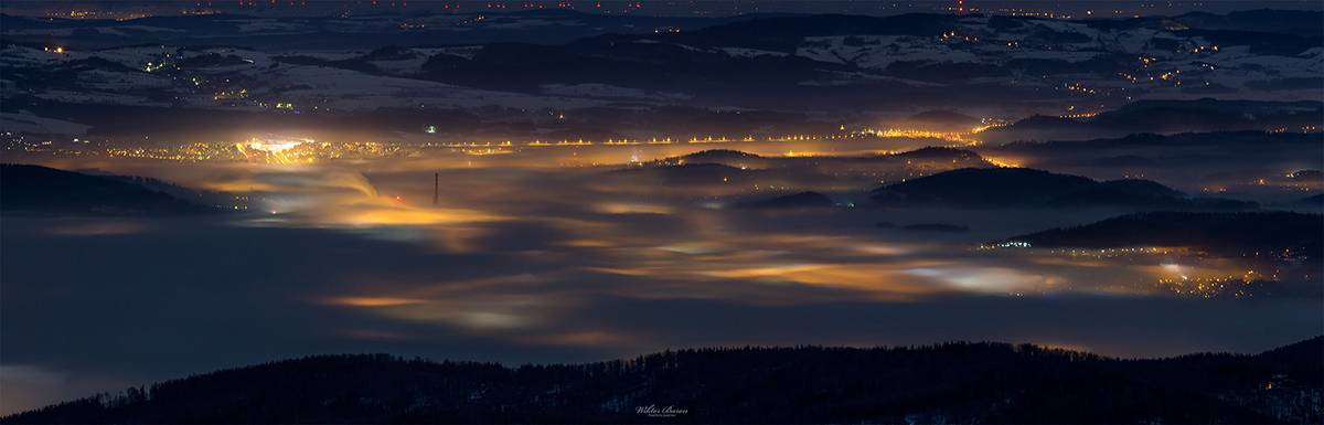 Panoramic view of lights below dark mountain ridges under a glowing night sky.