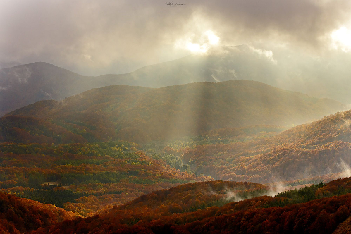 Sunbeams breaking through cloud above wooded autumn mountain slopes.