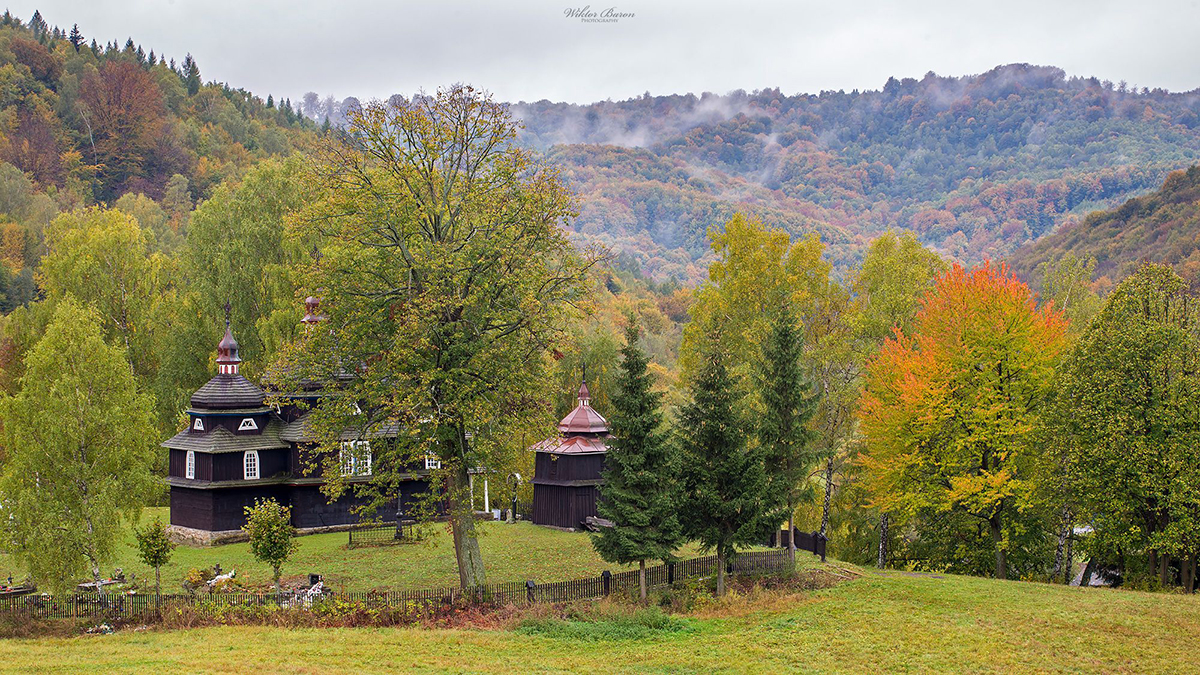 Two small wooden buildings beside trees with autumn foliage in a mountain valley.
