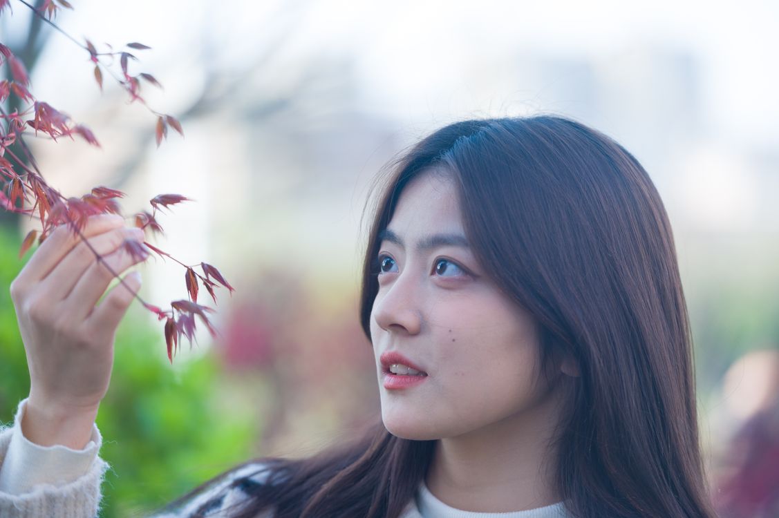 Woman looking at reddish leaves on a branch.