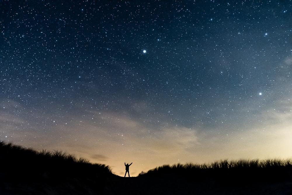 A small figure on a ridge beneath a star-filled sky at twilight.