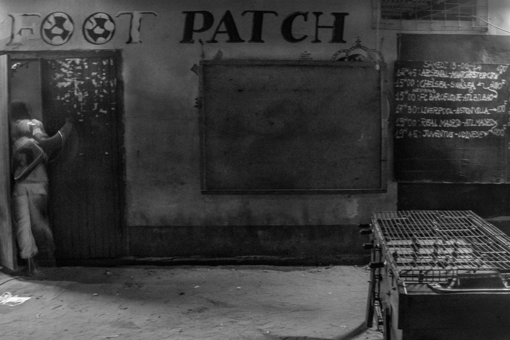 Street-side wall marked with the word 'PATCH' above a football fixtures board, with a person at the doorway.
