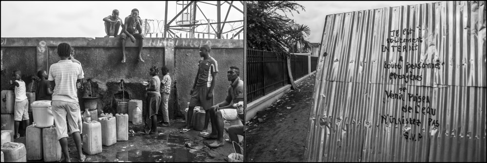 People standing among containers by a fence and bridge.