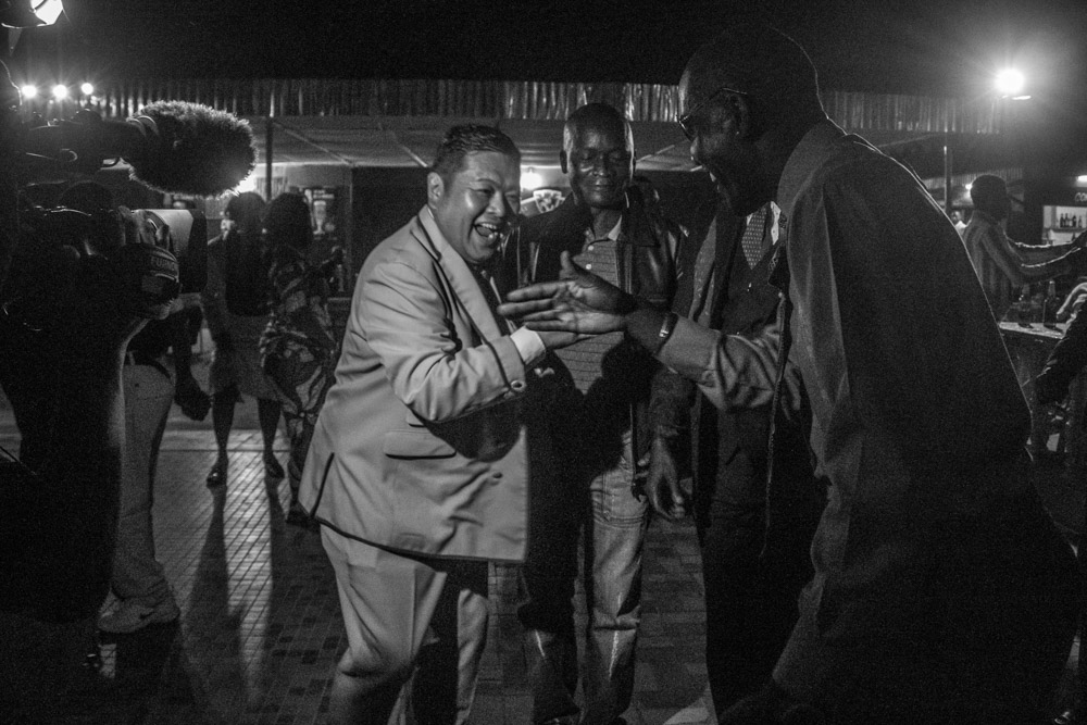 People gathered and speaking in a busy night street scene.