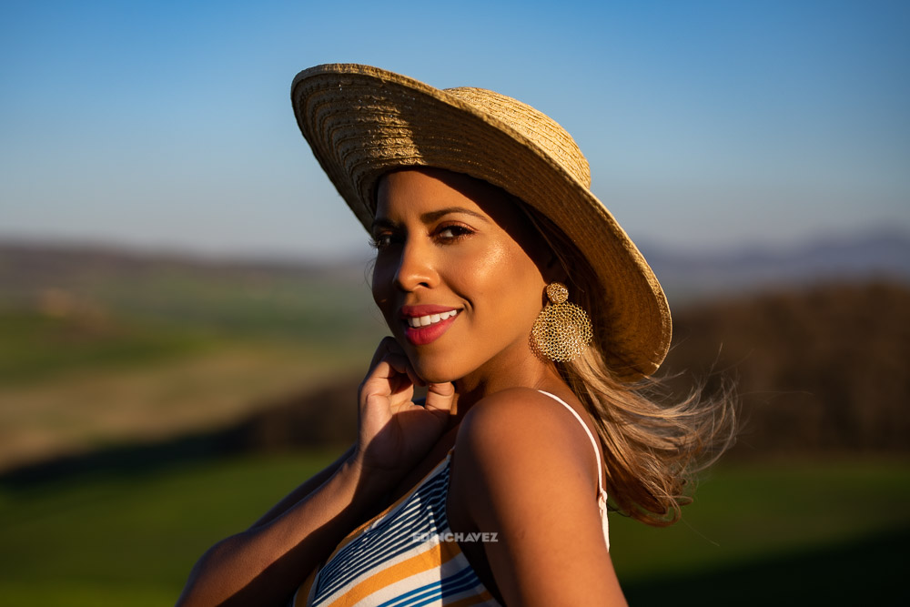 Golden hour portrait of a woman in a straw hat, warm evening light on her face and soft green hills behind her