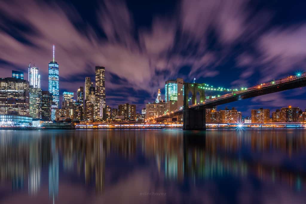 New York City skyline and bridge lights reflected across dark water at night