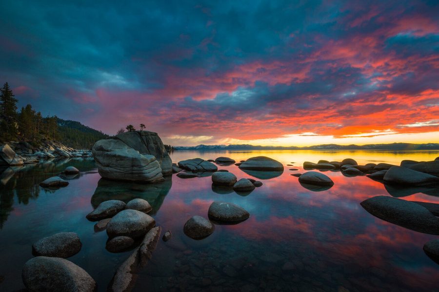 Boulders in still Lake Tahoe water reflecting a red, orange and teal sunset sky