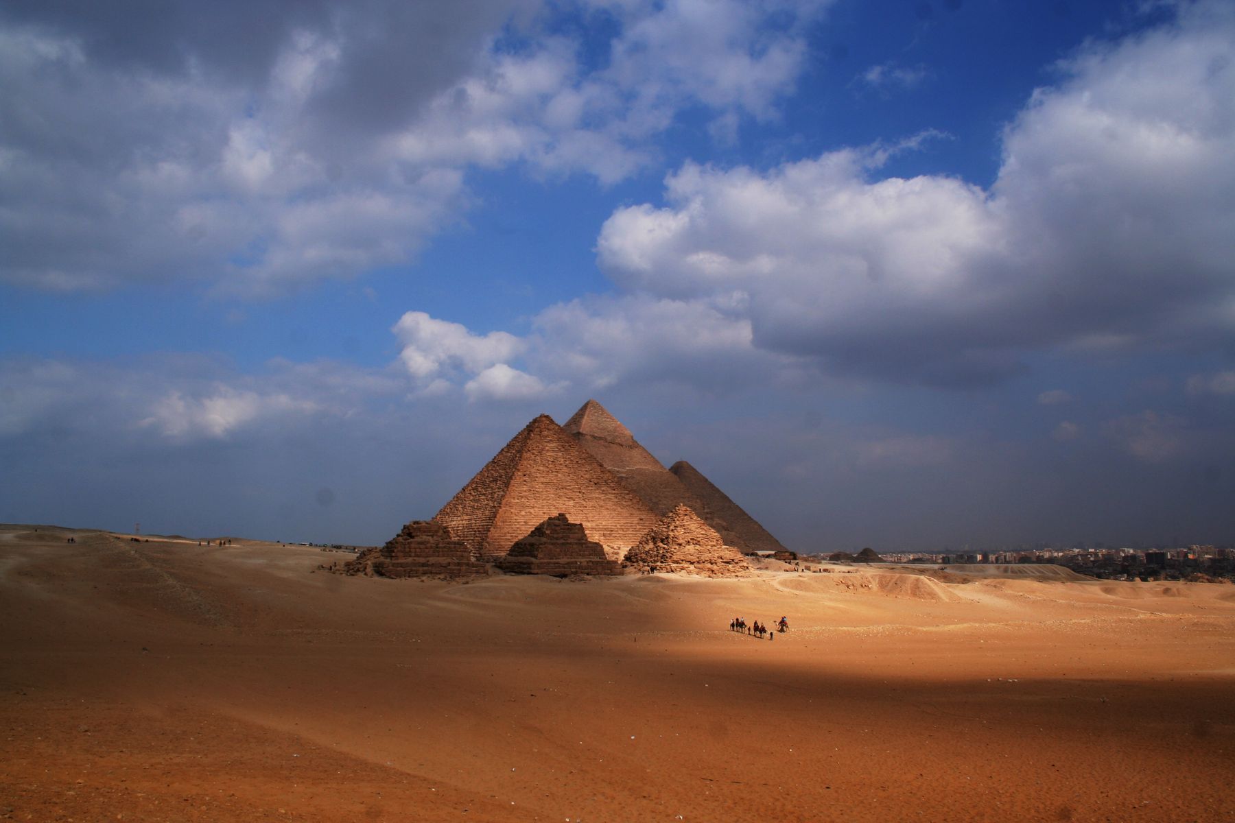 The Giza pyramids rising above desert dunes under a dramatic cloudy sky