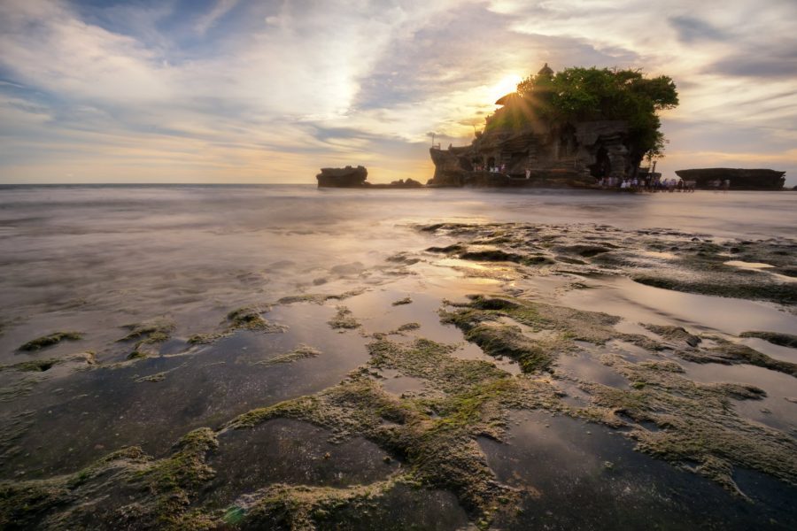 Tanah Lot sea temple on its rock at sunset with sun rays over the water