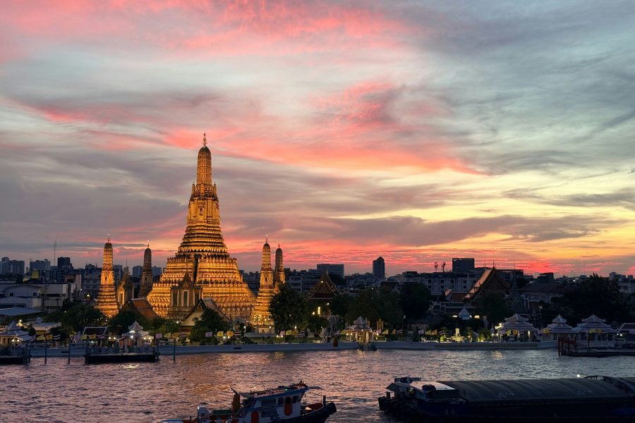 Wat Arun illuminated beside the Chao Phraya River under a pink sunset sky in Bangkok