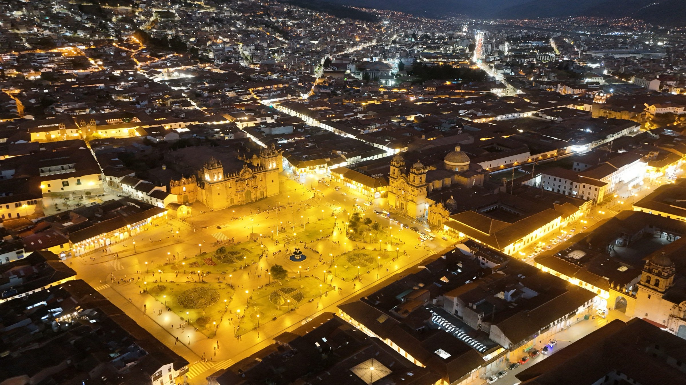 Cusco Plaza de Armas illuminated at night beneath surrounding city lights.