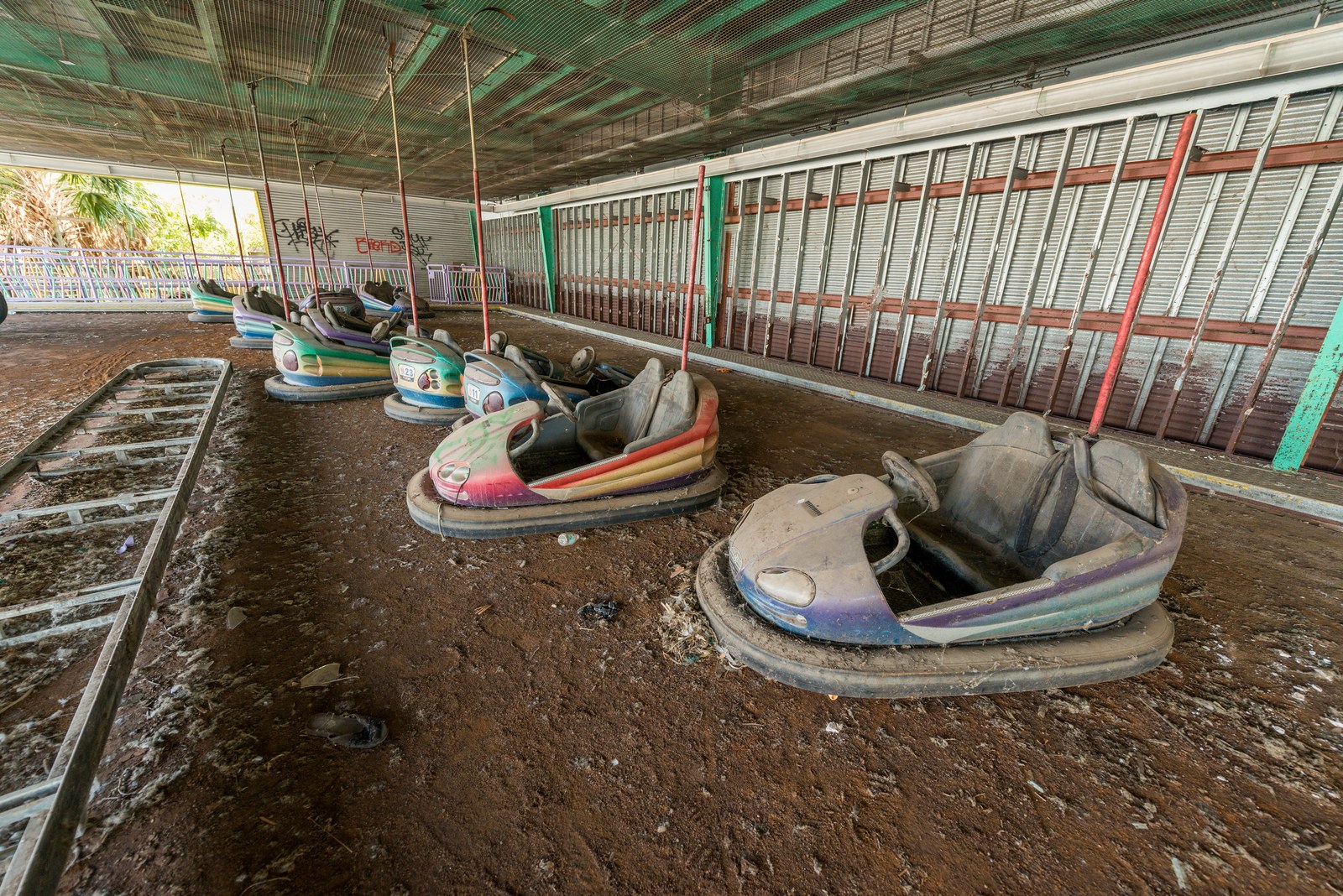 Weathered bumper cars covered in dust and peeling paint inside an abandoned amusement park