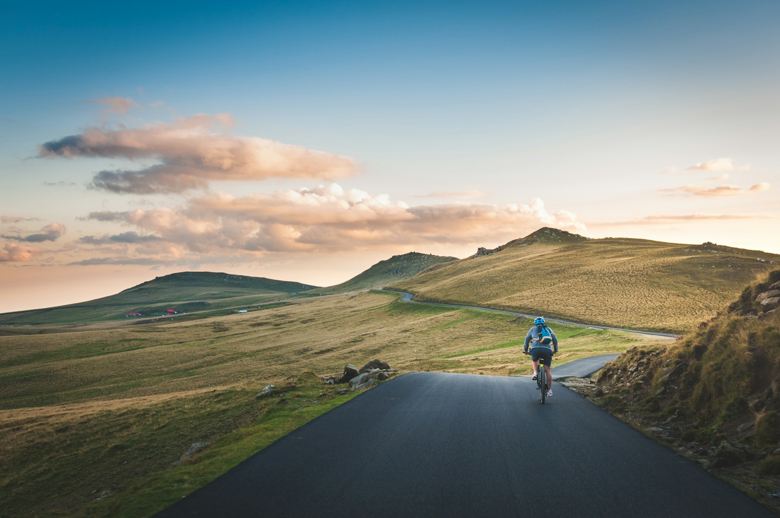 Lone cyclist riding a mountain road toward rolling hills at sunset