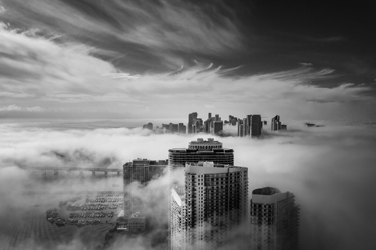 Black and white aerial view of the Miami skyline and Brickell Bay marina emerging from low fog, photographed by Edin Chavez