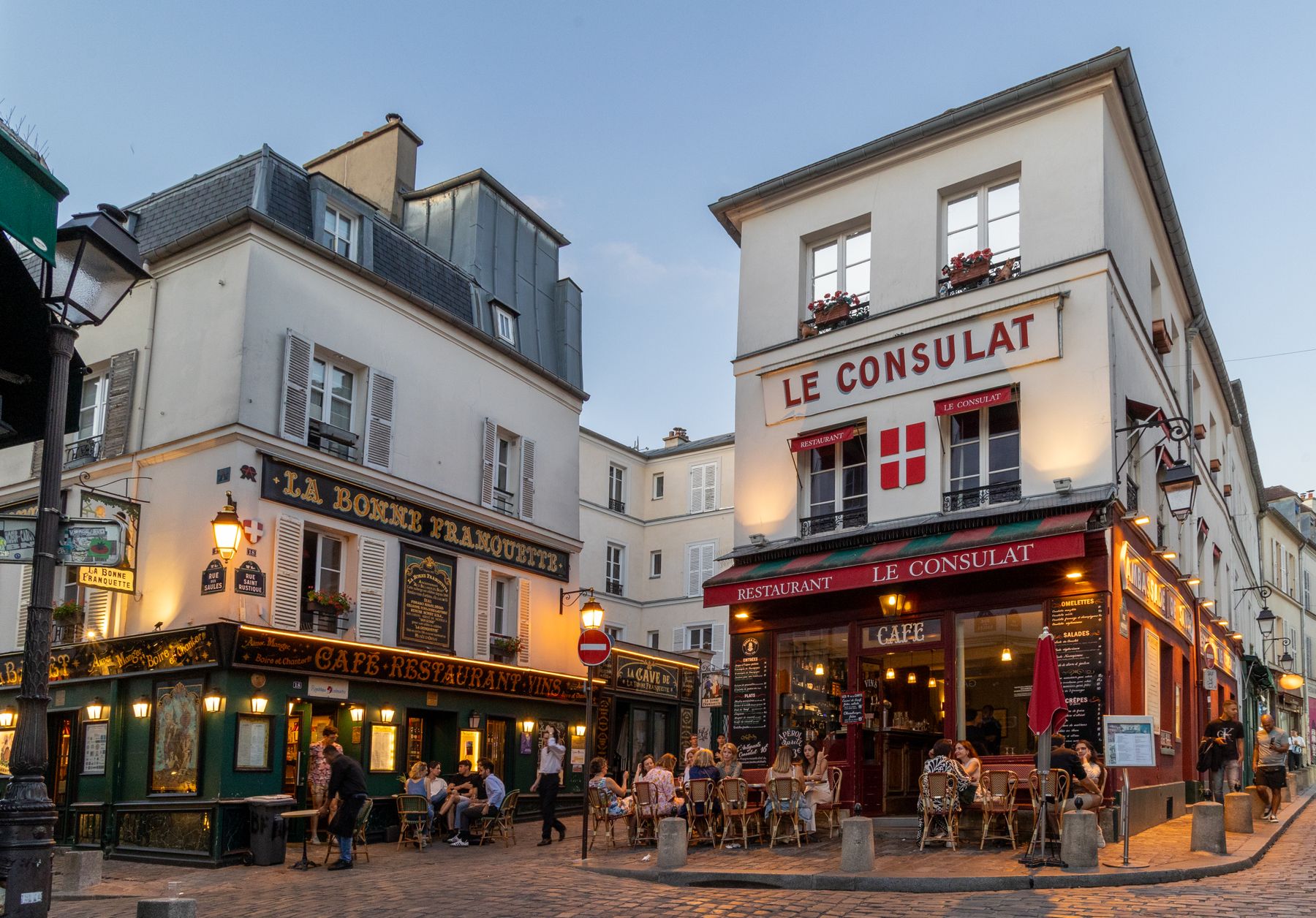 Le Consulat and La Bonne Franquette cafes on a cobbled Montmartre corner beneath a pale blue-grey sky