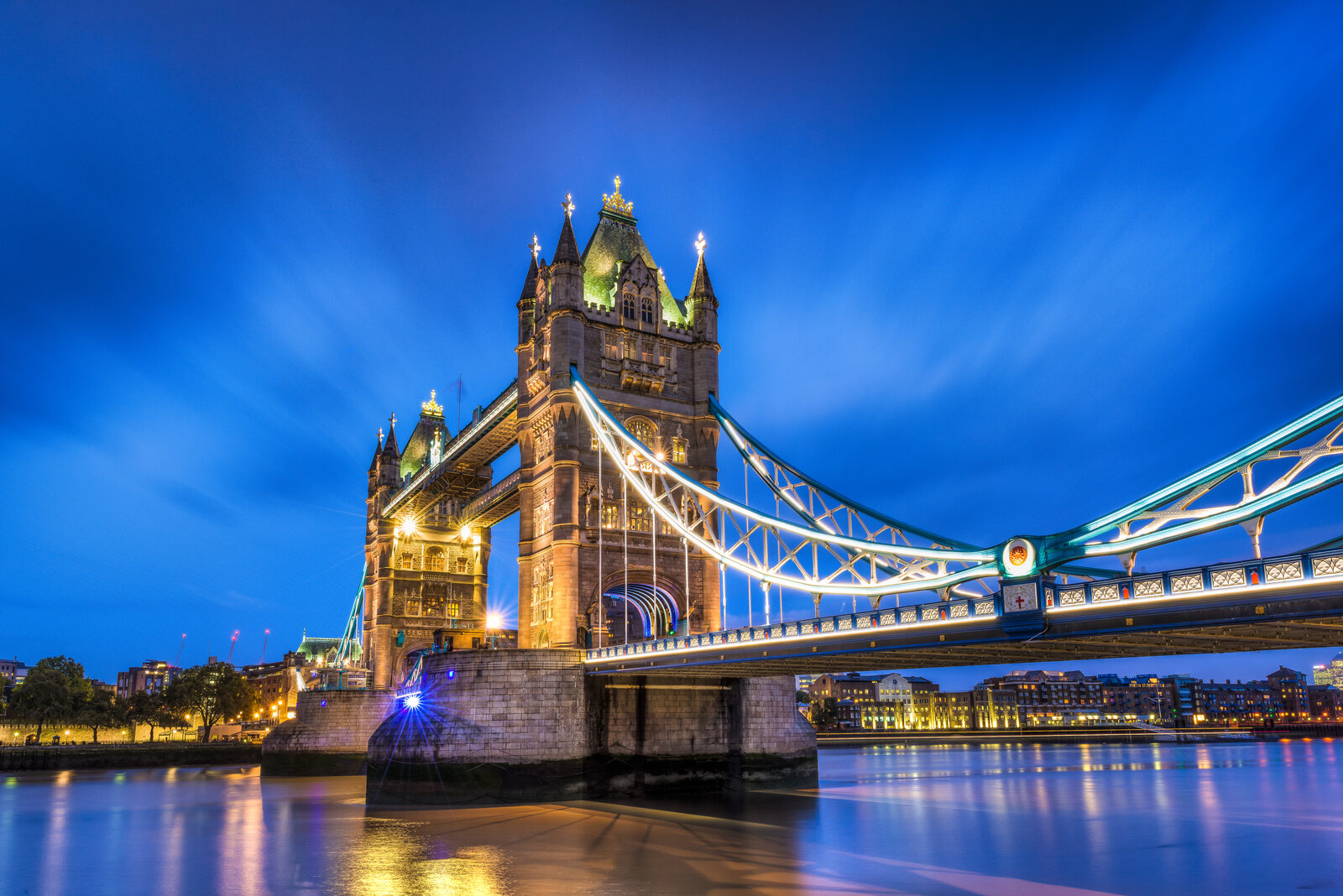 London skyline along the Thames with Tower Bridge lit at twilight beneath a deep blue sky