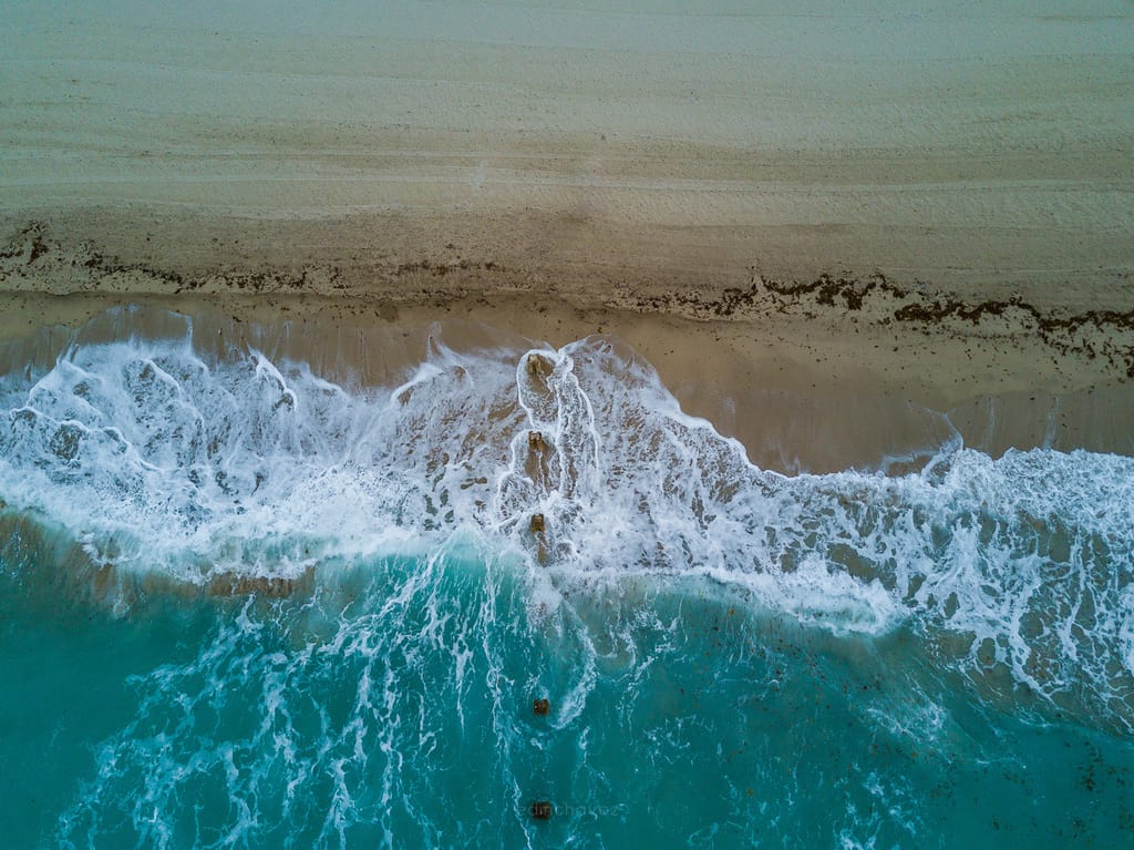 Turquoise surf breaking across a Miami Beach shoreline seen directly from above