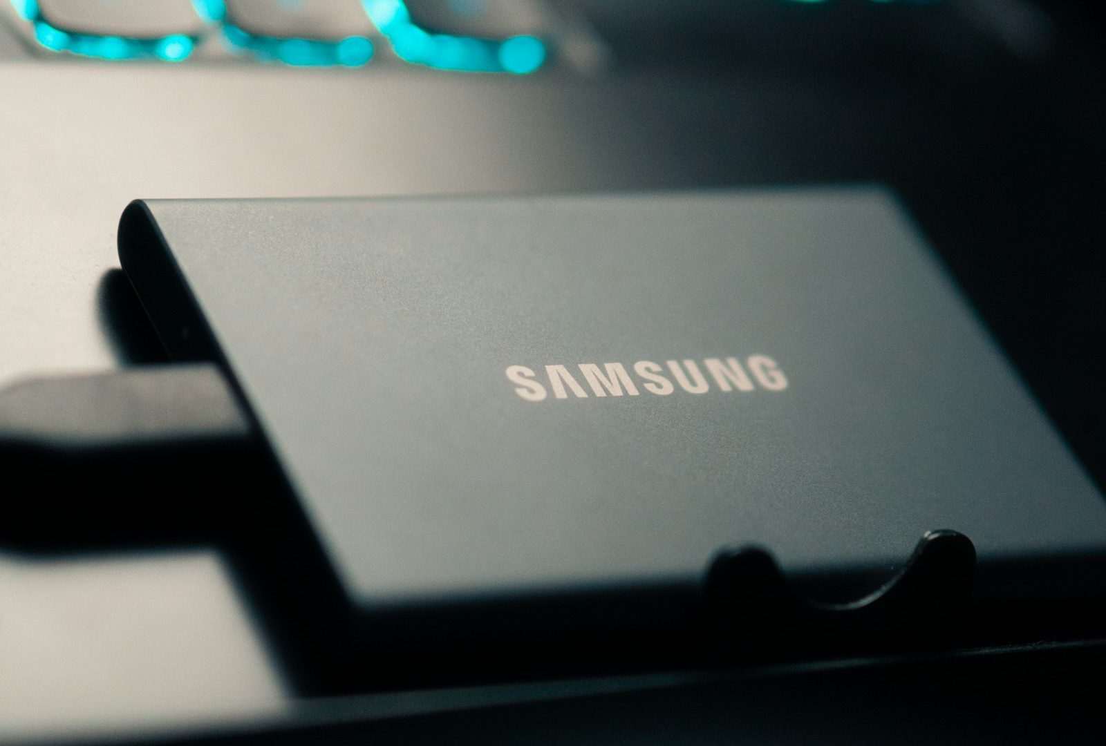 Samsung portable SSD connected beside a keyboard glowing blue, illustrating local photo storage for an online backup workflow